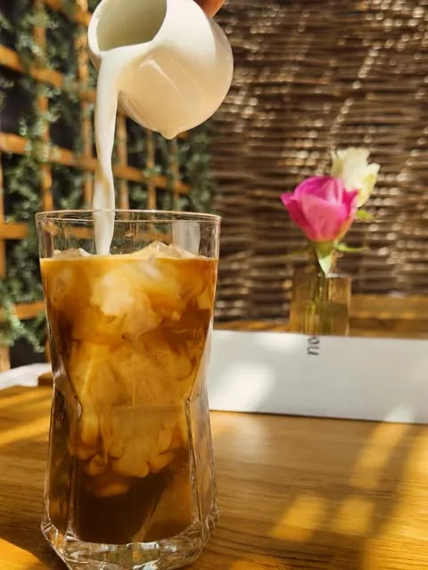 Milk being poured into iced coffee in the sunny café garden